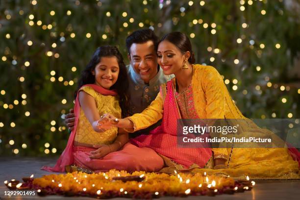 parents with their daughter placing diyas together - diwali family stock-fotos und bilder