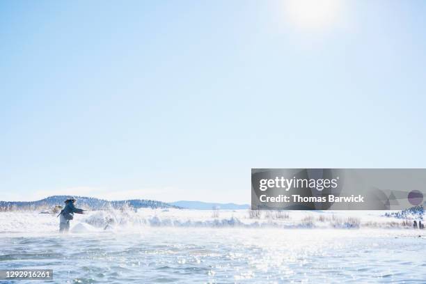 Female fly fisher wading and casting in river on winter morning