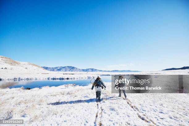 Female friends walking through snow to fly fishing stream on winter morning