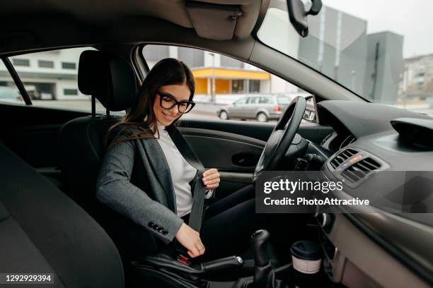 photo of a business woman sitting in a car putting on her seat belt - business car stock pictures, royalty-free photos & images