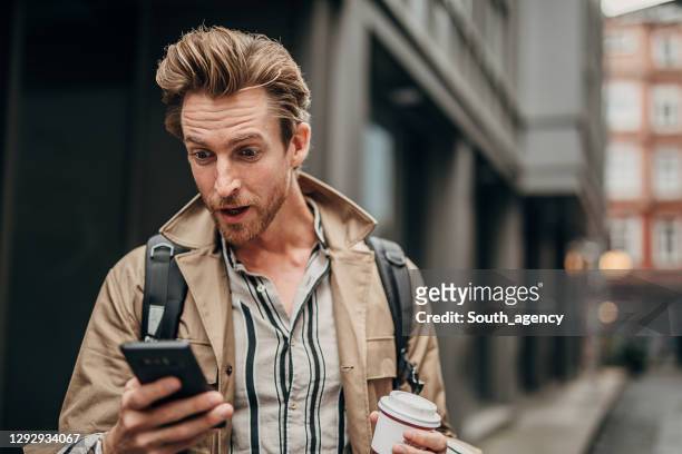 überraschter mann mit telefon auf der straße in der stadt - faszination stock-fotos und bilder