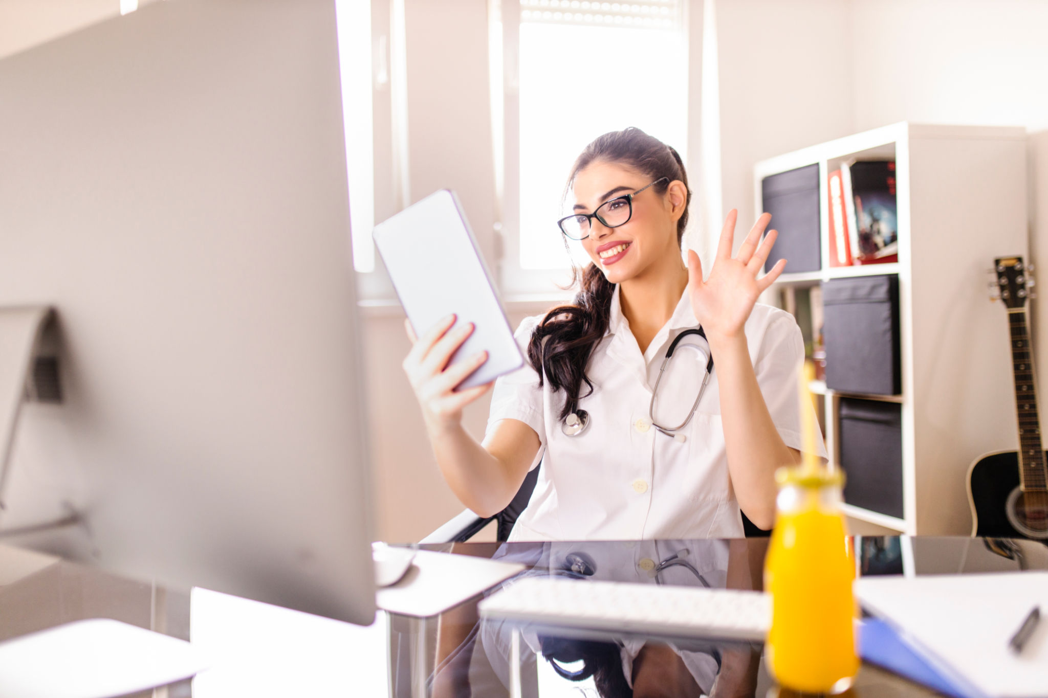 Médico trabalhando, tendo chamada de vídeo em tablet digital e bebendo suco de laranja no consultório Médico trabalhando, tendo chamada de vídeo em tablet digital e bebendo suco de laranja no consultório