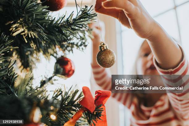 little girl carefully places christmas baubles onto a christmas tree - finishing touch stockfoto's en -beelden