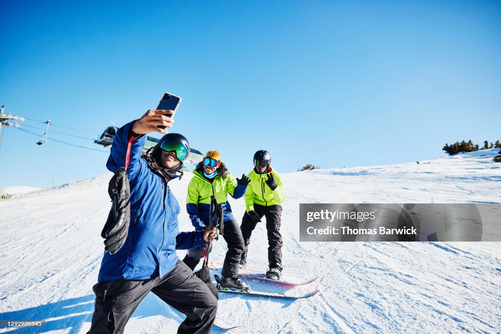 Man taking a selfie with friends at top of ski slope on sunny winter afternoon