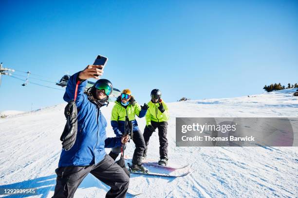 man taking a selfie with friends at top of ski slope on sunny winter afternoon - snowboarding stock pictures, royalty-free photos & images