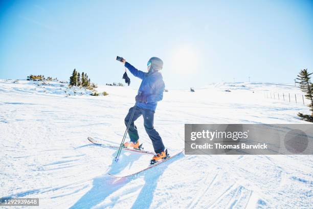 man taking a selfie with smart phone at top of ski slope on sunny winter afternoon - co op stock pictures, royalty-free photos & images