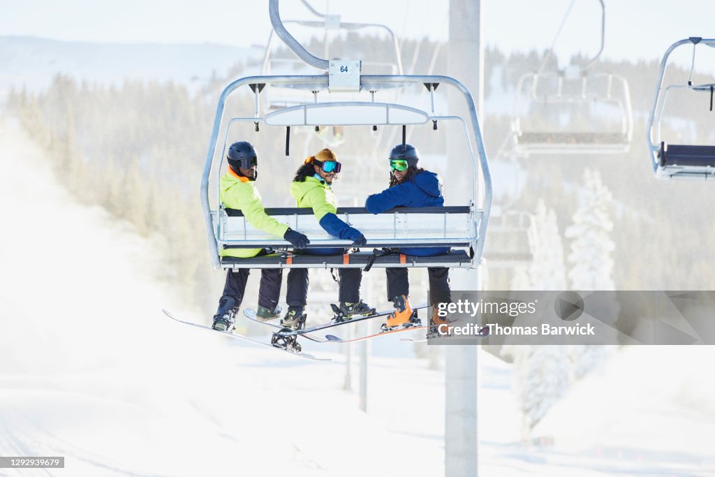 Smiling friends riding chairlift together while skiing and riding on sunny winter afternoon
