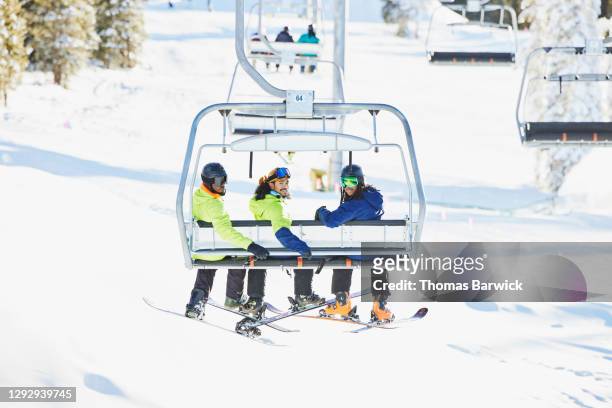 smiling friends riding chairlift together while skiing and riding on sunny winter afternoon - sport d'hiver photos et images de collection
