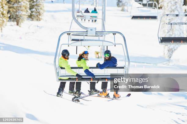 Smiling friends riding chairlift together while skiing and riding on sunny winter afternoon