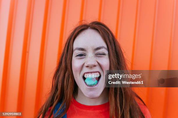 young woman chewing gum while standing against orange wall - kauwen stockfoto's en -beelden