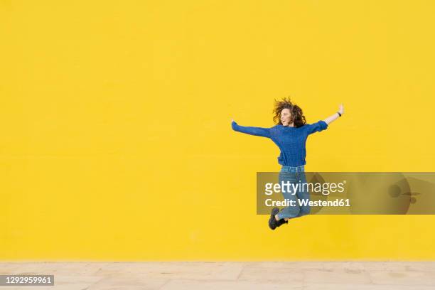 young woman jumping in the air in front of yellow background - gioia foto e immagini stock