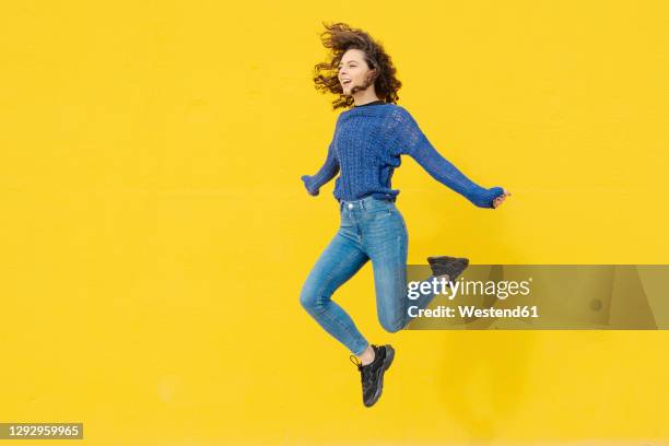 young woman jumping in the air in front of yellow background - gelber hintergrund stock-fotos und bilder