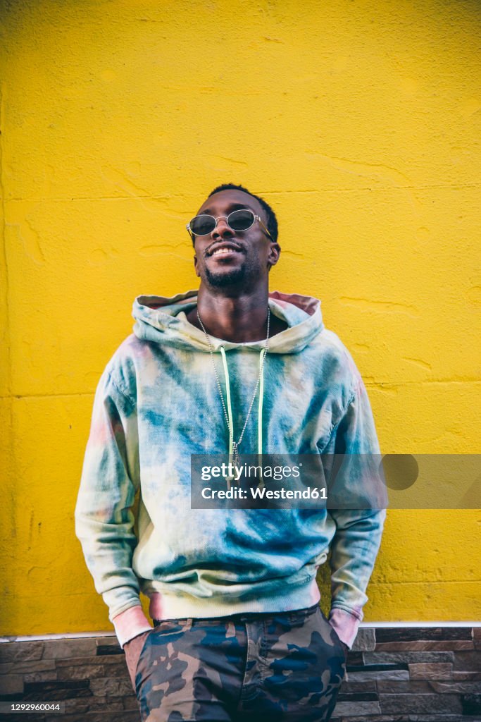 Portrait of young man with sunglasses leaning against yelow wall