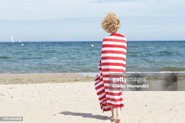 back view of young woman wrapped in beach towel standing in front of the sea - striped towel stock pictures, royalty-free photos & images