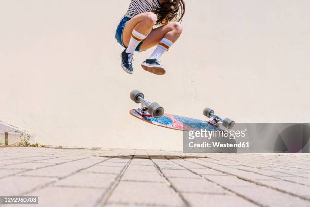 legs of young woman performing stunt on footpath against wall during sunny day - skating stock pictures, royalty-free photos & images