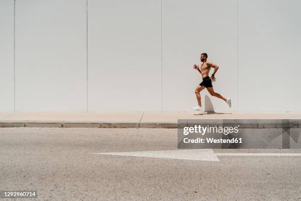 barechested male athlete running on pavement with arrow sign on the road - sin camisa fotografías e imágenes de stock