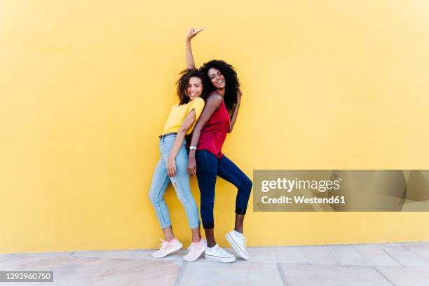 cheerful girlfriends enjoying while standing back to back by yellow wall - girlfriend stock pictures, royalty-free photos & images