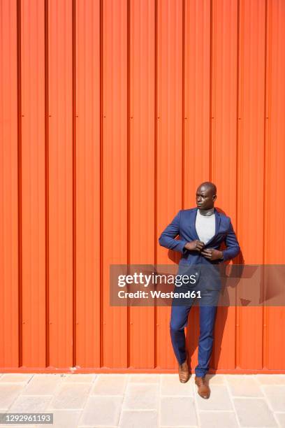 portrait of businessman wearing blue suit and grey turtleneck pullover standing in front of orange wall - black turtleneck stock pictures, royalty-free photos & images