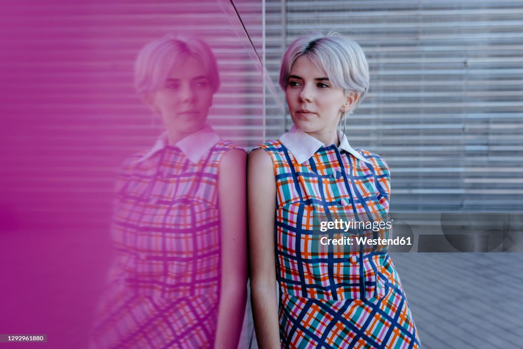 Thoughtful young woman with short hair standing by pink glass wall