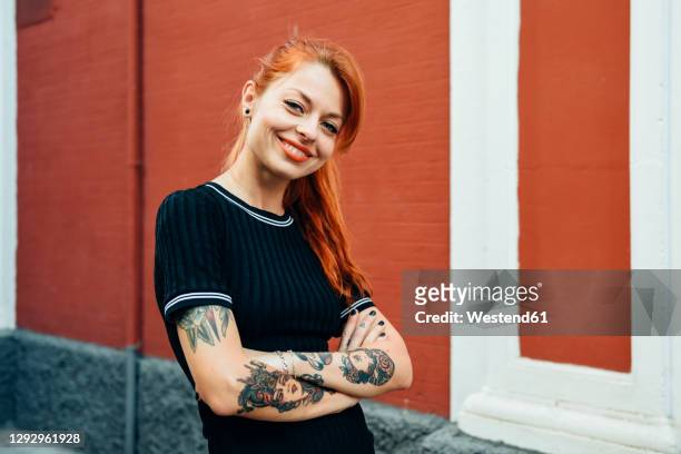 portrait of smiling red-haired tattooed woman standing in the city - tatouage femme photos et images de collection