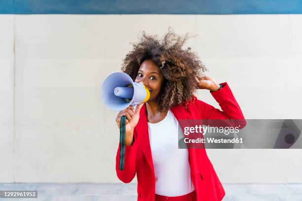 mid adult woman using megaphone while standing against wall - megafon stock-fotos und bilder