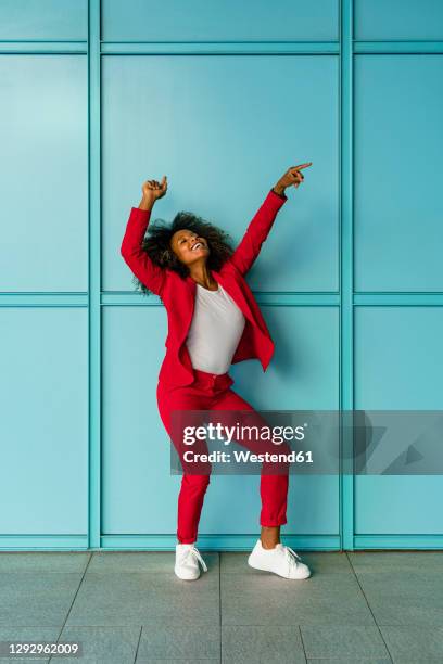 mid adult woman cheerfully dancing against wall - blue dress fotografías e imágenes de stock