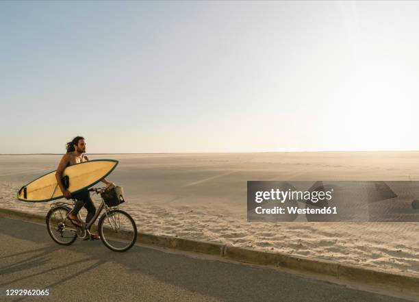 surfer riding a bicycle during the sunset in the beach, costa nova, portugal - carrying bike stock pictures, royalty-free photos & images