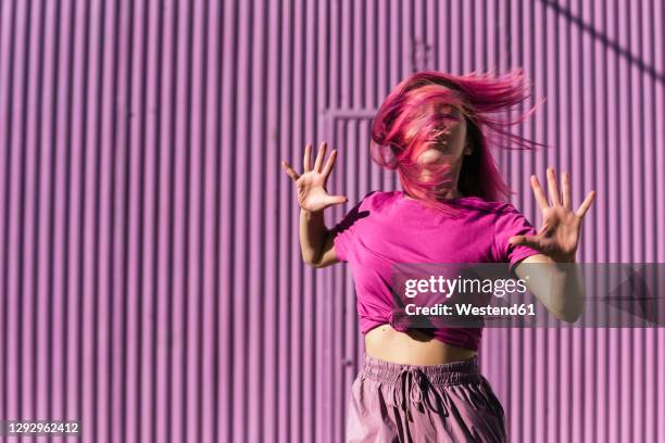 young woman with dyed red hair dancing in front of purple wall in the city - dyed red hair fotografías e imágenes de stock