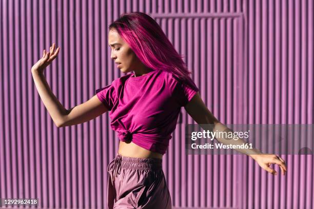 young woman with dyed red hair dancing in front of purple wall in the city - dyed red hair fotografías e imágenes de stock