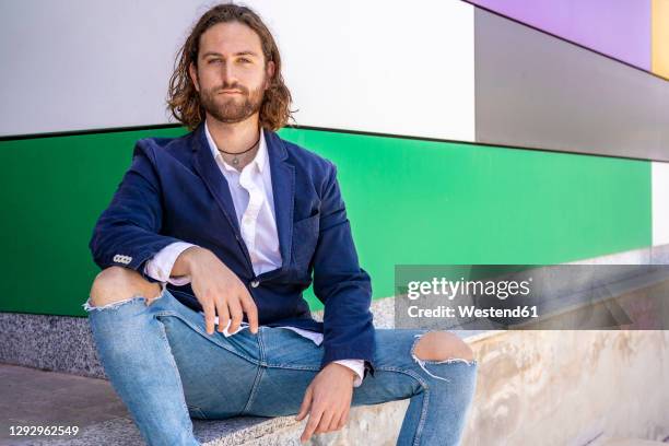 confident fashionable businessman sitting against colorful wall - ripped jeans bildbanksfoton och bilder