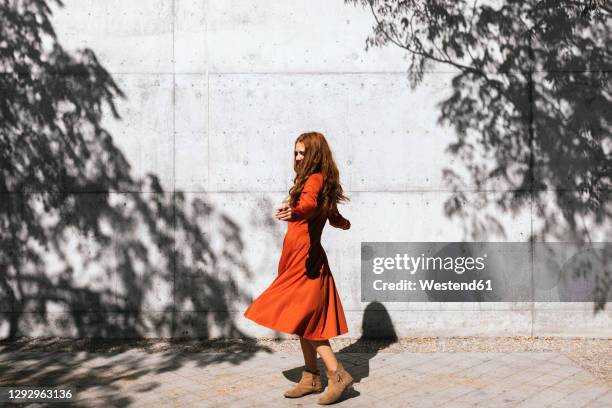 young woman with arms outstretched spinning against tree shadow wall - rotes kleid stock-fotos und bilder