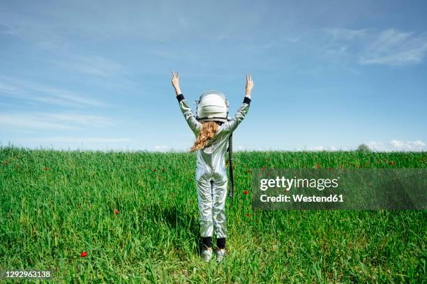 rear view of girl in astronaut costume standing with peace sign on grass - astronaut helm stock-fotos und bilder