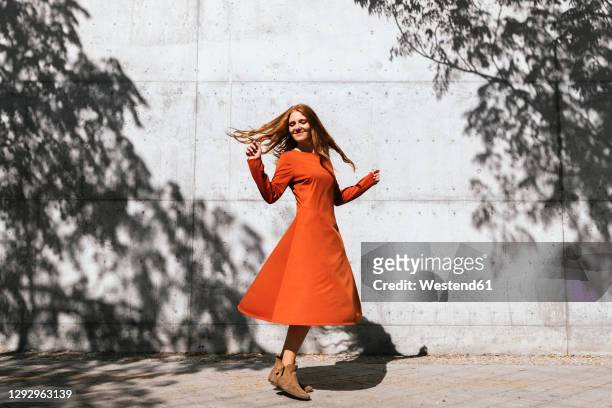 happy woman dancing against tree shadow wall - vestito da donna foto e immagini stock