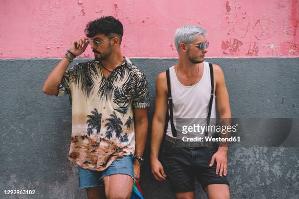 gay couple lookig sideways in front of pink and grey wall - short hair photos et images de collection