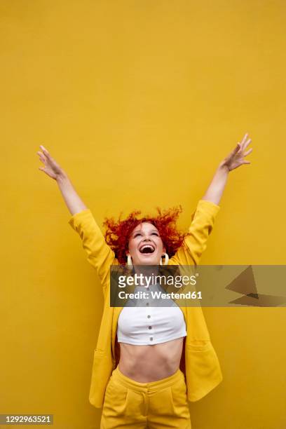 exuberant young woman with red curly hair laughing in front of yellow wall - vestito multicolore foto e immagini stock