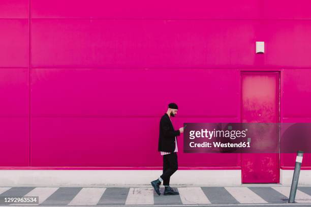 businessman using smartphone and walking along a pink wall - lila stockfoto's en -beelden