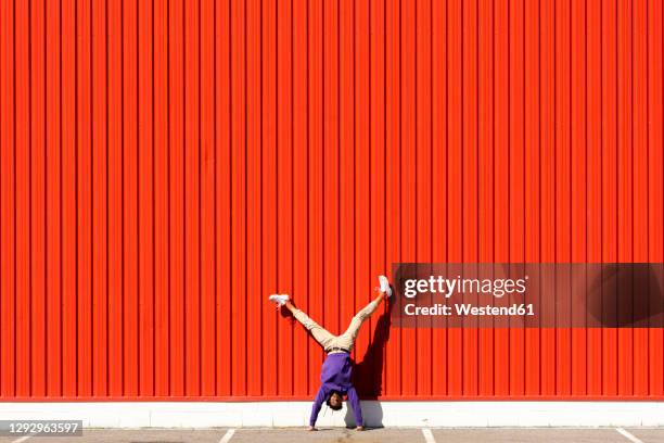 young man doing a handstand at a red wall - flexible fotografías e imágenes de stock