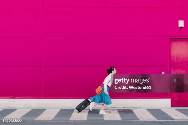 young woman with smartphone running with trolley along a pink wall - wheeled luggage 個照片及圖片檔