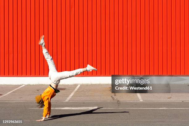 young woman doing a handstand in front of a red wall - handstand fotografías e imágenes de stock