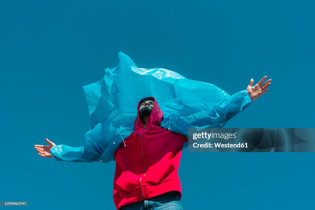 Young man wearing plastic rain coat, stanind in gthe wind with arms outstretched
