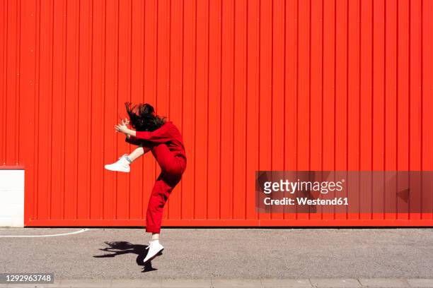 woman dressed in red overall jumping in the air in front of red roller shutter - tänzerin stock-fotos und bilder