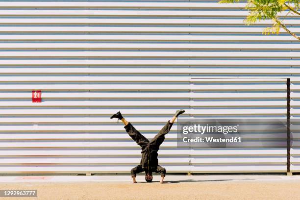 man wearing black overall doing handstand in front of industrial building - slide tackle stock pictures, royalty-free photos & images