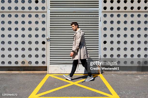 impatient man walking in yellow marked area in front of concrete wall - trench coat stock pictures, royalty-free photos & images