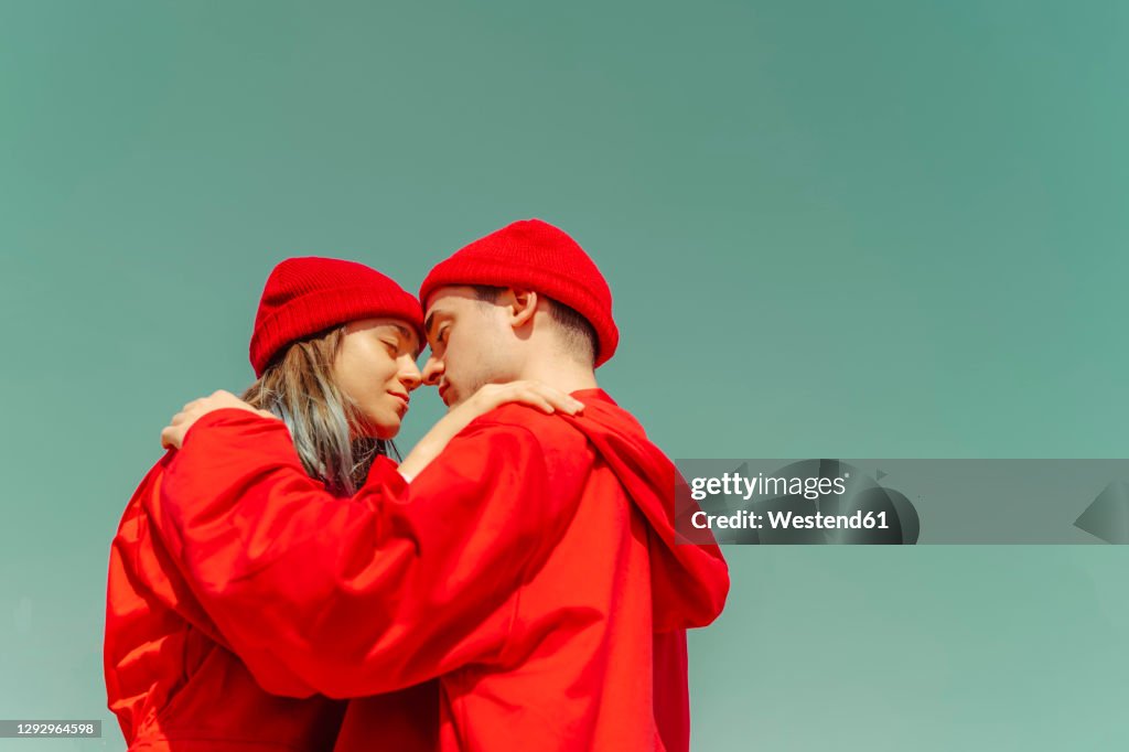 Young couple wearing red overalls and hats standing head to head against sky