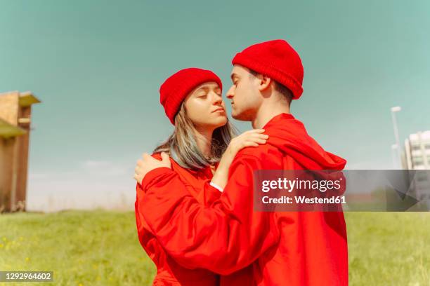 young couple wearing red overalls and hats standing on a meadow - wear red day - fotografias e filmes do acervo