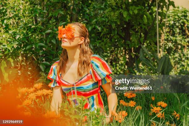 woman in nature wearing glasses with orange flowers covering her eyes - odd one out obscure stock pictures, royalty-free photos & images