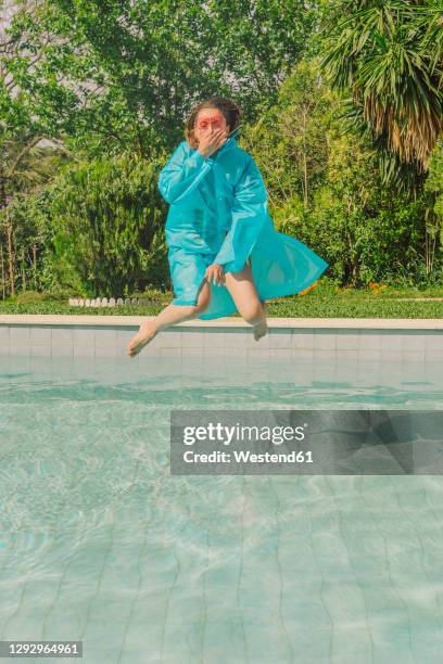 woman in blue rain coat jumping into swimming pool - holding nose stock pictures, royalty-free photos & images