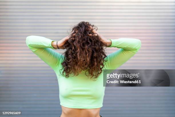 young woman wearing green crop top with hands in hair posing against gray wall - wavy hair stock pictures, royalty-free photos & images