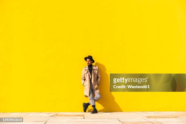 young man dancing in front of yellow wall - trench coat stock pictures, royalty-free photos & images