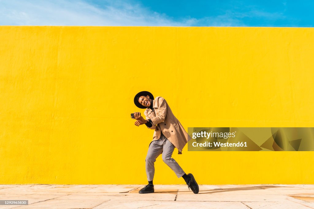 Young man dancing in front of yellow wall, taking selfies